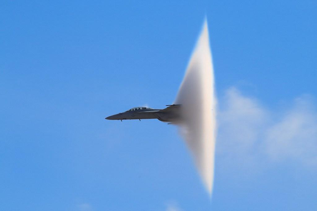 An F/A-18 in a vapor cone against a clear blue sky